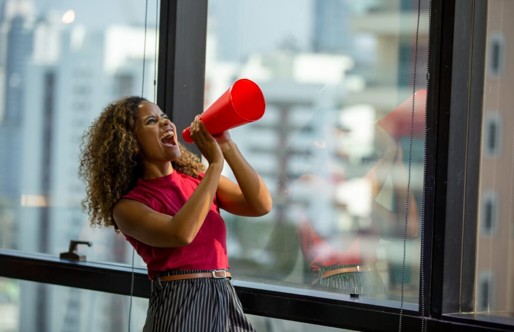 woman in red top screaming passionately into an ineffective-looking megaphone - Dive into the world of Pay-Per-Click (PPC) advertising and learn how to craft a successful PPC campaign for your business. This post guides you through audience understanding, keyword selection, compelling ad copy, landing page optimization, and continuous campaign monitoring for business growth. - What factors contribute to the success of a pay-per-click campaign? - your wp guy