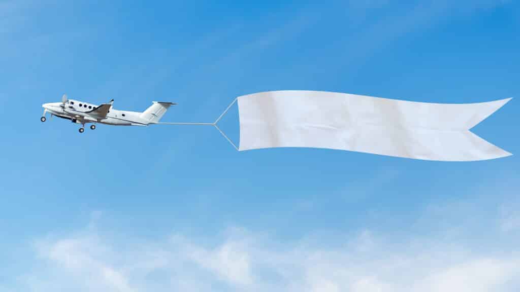 Plane flies in the sky with a white banner for ad.